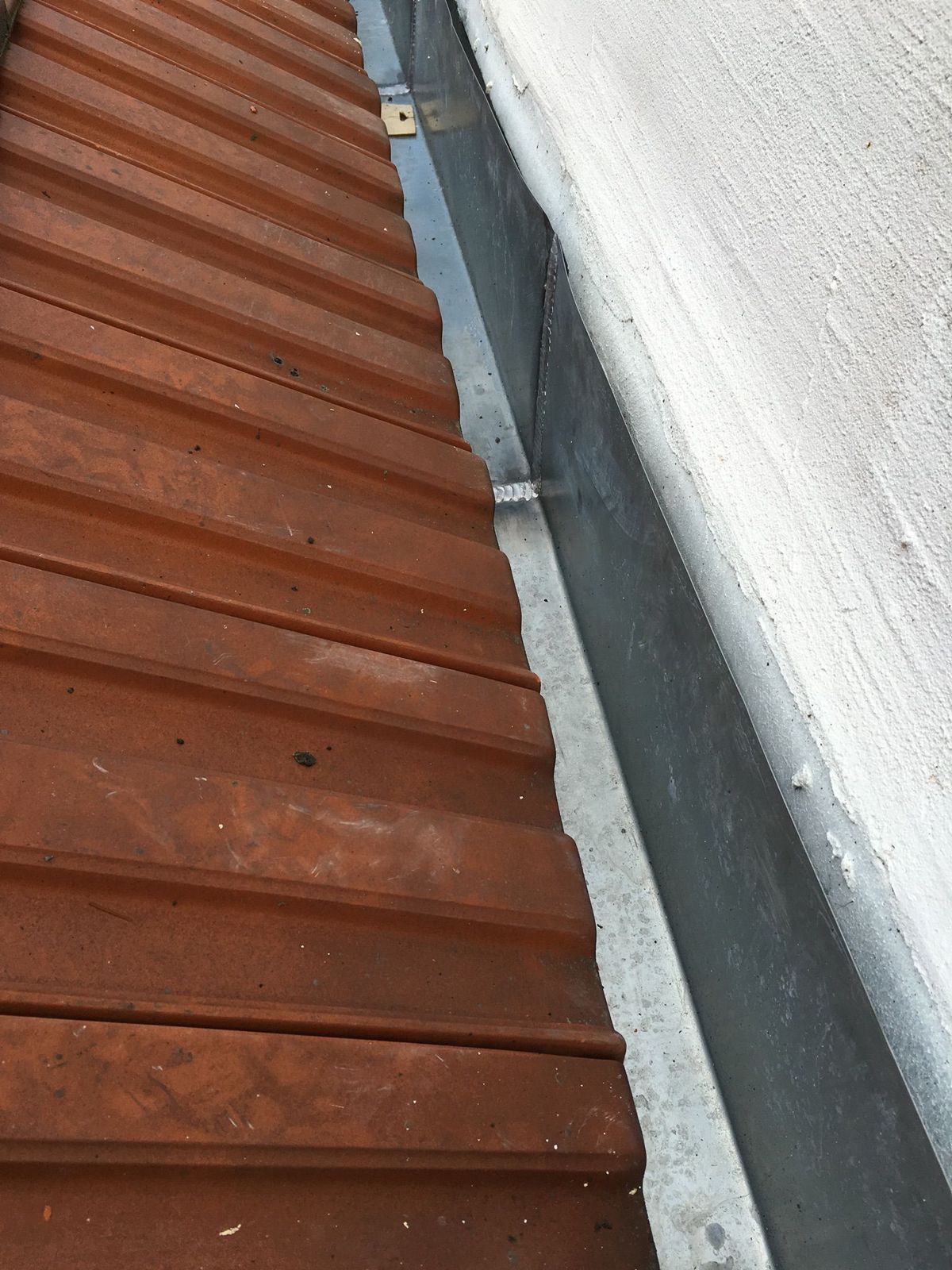 Rive en zinc entre un mur et une toiture en tuiles